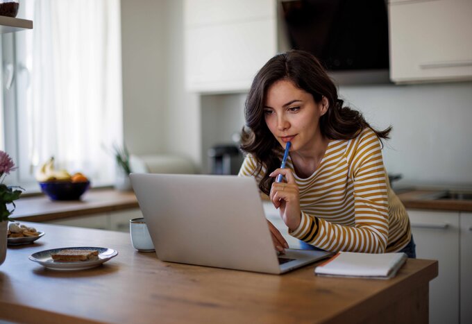 Femme accoudée à un comptoir regardant un ordinateur - Communiquer avec nous - Ellipse Assurances